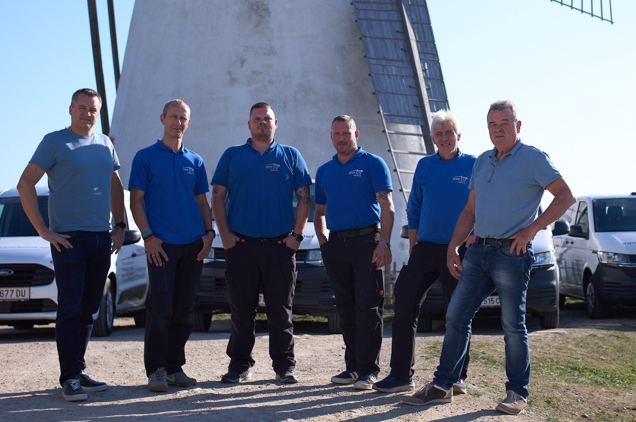 Sechs Mitarbeiter von schiener technik vor der Retzer Windmühle, dahinter die Servicefahrzeuge